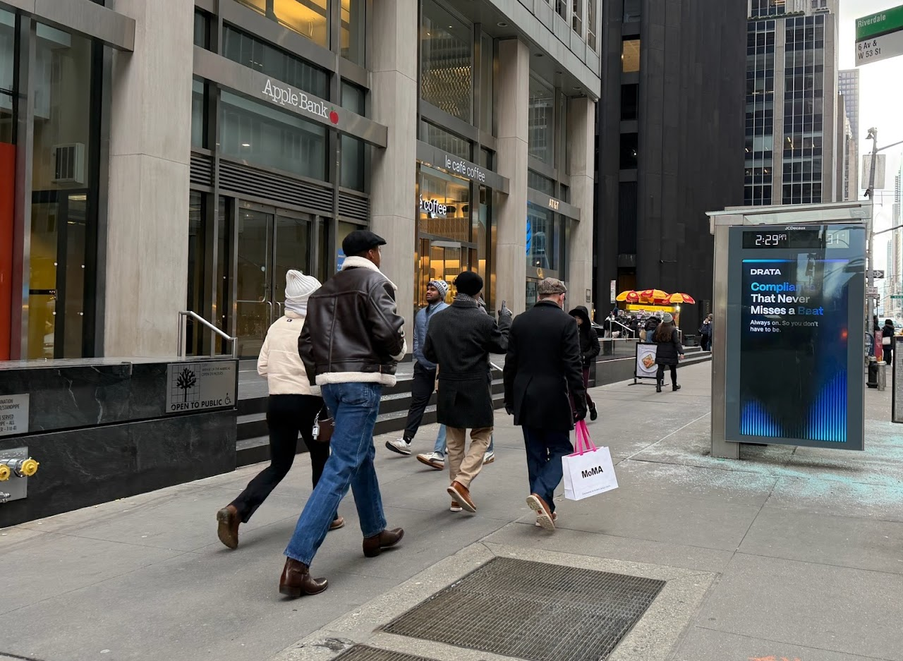Drata 'Compliance That Never Misses a Beat' urban panel beside Apple Bank on 6th Ave & W 53rd St, Midtown Manhattan