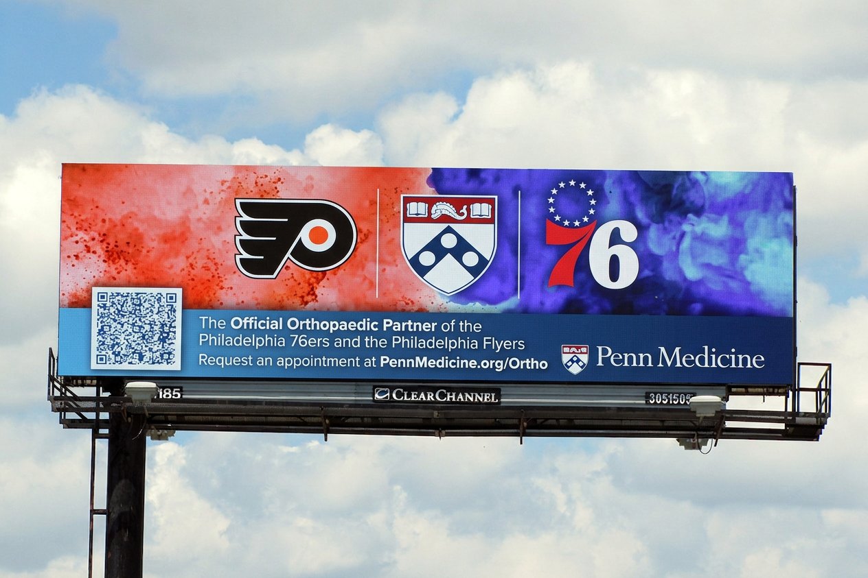 A digital billboard mockup showing a Penn Medicine orthopedics ad naming Penn Medicine as the official orthopaedic partner of the Philadelphia 76ers and Flyers, with a request-an-appointment prompt.