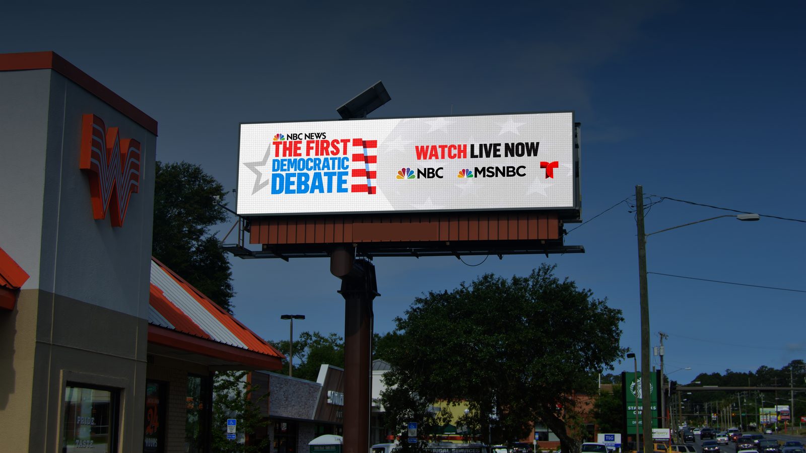 A roadside digital billboard promoting national debate-night television coverage, reading The First Democratic Debate, Watch Live Now.